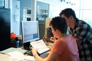 Two people transcribing from a paper sheet into a computer based system